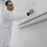 Male scientist writing complex chemical formula on whiteboard in lab.