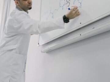 Male scientist writing complex chemical formula on whiteboard in lab.