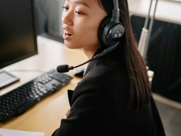 Asian woman using headset for customer support in a modern office.