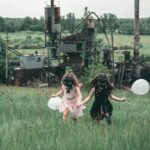 Two children wearing gas masks run with balloons near an industrial site.
