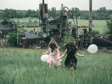 Two children wearing gas masks run with balloons near an industrial site.