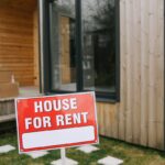 A modern wooden house with a bold 'House for Rent' sign on a grassy lawn, showcasing rental opportunity.