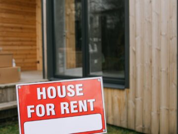 A modern wooden house with a bold 'House for Rent' sign on a grassy lawn, showcasing rental opportunity.
