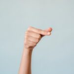 A woman's hand making a gesture against a calm blue background, symbolizing communication.
