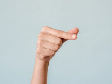 A woman's hand making a gesture against a calm blue background, symbolizing communication.