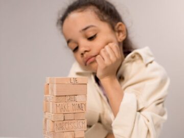 A young girl contemplates a stack of wooden blocks with words like 'lie' and 'kindness.'