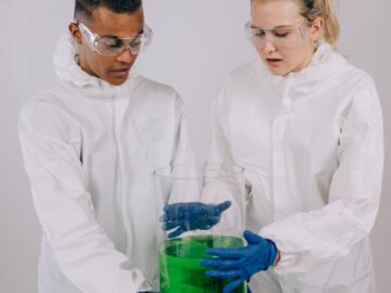 Two scientists in protective gear conducting an experiment with a green chemical solution in a laboratory.