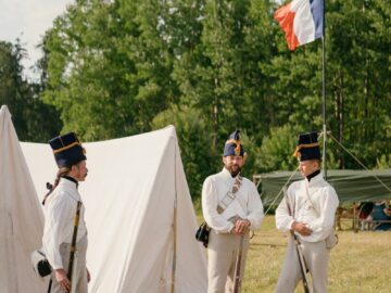 Historical reenactment with French soldiers in period uniforms holding muskets by tents.