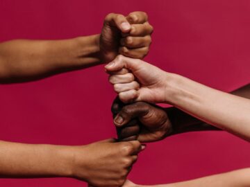 Close-up of diverse hands forming fists, symbolizing unity and teamwork on a vivid pink background.