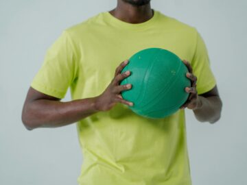 Unrecognizable man in yellow shirt holding a green ball against a white background.