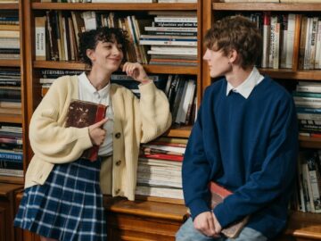 Two students enjoy a moment in a warm library environment, showcasing friendship and learning.