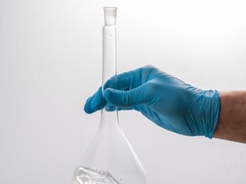 Close-up of a gloved hand holding a volumetric flask in a scientific laboratory setting.
