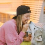 Young woman joyfully bonding with her Siberian Husky outdoors, sharing a treat.