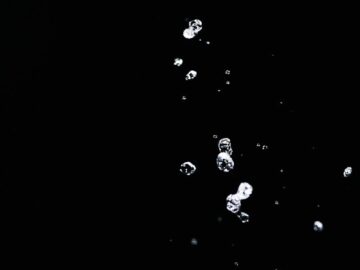 Close-up of water droplets captured mid-air against a stark black background, highlighting fluid motion and texture.