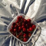 Fresh cherries in a plastic container on a shiny surface, capturing the essence of summer.
