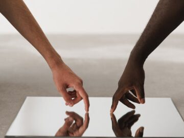 Two hands of different ethnicities touching and reflecting on a minimalist mirror.