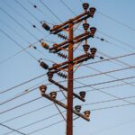 Close-up of a high voltage utility pole with transmission lines against a clear blue sky.