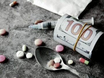 Symbolic representation of drug addiction and financial cost with pills and money.