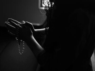 silhouette of woman holding rosary while praying