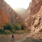 a man walking down a dirt road next to a mountain