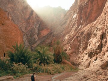 a man walking down a dirt road next to a mountain