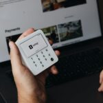 A person holding a cell phone in front of a laptop